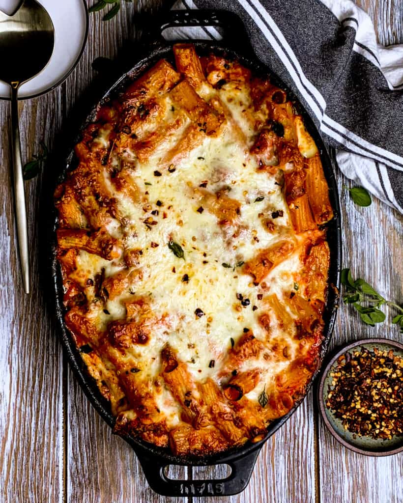 Bake rigatoni with pepper jack and mozzarella cheese, marinara sauce, topped with red pepper flakes in black dish.